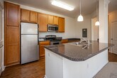 Located at 1000 Bridgeway Dr in Maryville, Tennessee, this single-floor residence offers a well-designed layout that balances comfort and functionality. The spacious living area is a standout feature, boasting plush carpeting, crown molding, and a ceiling fan with light fixture. A bay-style wall of windows and a glass exterior door flood the room with natural light, creating a warm and inviting atmosphere with views of the surrounding area. The kitchen is equipped with warm honey-toned cabinetry, dark granite-style countertops, stainless steel appliances including a gas range and built-in microwave, and a white refrigerator. A peninsula counter adds additional prep space and visual separation from the adjoining area. Hardwood-style flooring flows through the kitchen, hallways, and bathrooms, adding a cohesive and polished look. The bedrooms are carpeted and include ceiling fans and generous closet space with built-in shelving. The bathrooms feature warm wood vanities topped with dark stone-style counters, large mirrors, and hardwood-style flooring. A dedicated laundry area accommodates a full-size washer and dryer, adding everyday convenience. Throughout, the interior is finished in crisp white and neutral tones, contributing to an open and clean aesthetic.