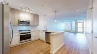 Located in the heart of downtown Phoenix, this thoughtfully designed residence offers a contemporary open-concept layout with a seamless flow between the kitchen and living room. The kitchen is a standout feature, showcasing a large stone-topped island with pendant lighting overhead, stainless steel appliances including a gas range, microwave, dishwasher, and refrigerator, complemented by a marble-style backsplash and a mix of white and wood-toned cabinetry. Light wood-style flooring runs throughout, lending warmth and continuity to the space. The living area is bathed in natural light, courtesy of expansive floor-to-ceiling windows and a glass door that opens to a private balcony with panoramic views of the Phoenix skyline. The primary bathroom is generously proportioned, featuring large-format tile flooring, a dual-sink vanity with ample cabinetry, a glass-enclosed shower, and a soaking tub. A secondary bathroom provides additional convenience. A dedicated walk-in closet with built-in wire shelving offers practical storage. The hallway connects all areas efficiently, completing a well-organized and modern urban living experience.