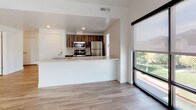 This contemporary single-floor unit offers a clean, modern aesthetic throughout, characterized by crisp white walls, warm wood-tone luxury vinyl plank flooring in the main living areas, and plush neutral carpet in the bedrooms. The entry foyer welcomes you with light hardwood-style flooring and a secure front door, leading seamlessly into the open-concept living and dining space. Large floor-to-ceiling windows and sliding glass doors flood the main living area with abundant natural light and offer pleasant outdoor views of surrounding greenery, complemented by a ceiling fan for added comfort. The kitchen is defined by a functional peninsula with a white quartz countertop, dark wood cabinetry, and a full suite of stainless steel appliances including a refrigerator, microwave, and gas range. The bedrooms are generously proportioned, each outfitted with ceiling fans and windows dressed with blinds that invite natural light. Two full bathrooms serve the unit — one featuring a single-sink vanity with wood-toned cabinetry, white quartz countertop, and a soaking tub with shower combination, and the other offering a crisp all-white tub-shower surround with chrome fixtures. The overall ambiance is bright, clean, and move-in ready.