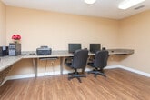 Located at 2754 Cumberland Blvd SE in Smyrna, Georgia, this single-floor business center offers a functional and well-appointed workspace designed to meet a variety of professional needs. The space features warm, neutral-toned walls paired with durable wood-look flooring throughout, creating a clean and practical environment.

The main area is anchored by an L-shaped, built-in workstation finished with granite-style countertops, providing generous desk space along multiple walls. Multiple computer workstations with monitors, keyboards, and office chairs are arranged to accommodate several users simultaneously, making the space well-suited for shared or collaborative work. Additional built-in counter sections extend along the walls, offering supplemental workspace for productivity.

Overhead, bright flush-mount fluorescent lighting ensures thorough illumination across the entire room, supporting extended use throughout the day. A textured ceiling adds a subtle design detail to the otherwise streamlined interior. A glass-paned interior door connects the workspace to an adjacent corridor, hinting at additional facilities nearby, including what appears to be a hallway leading to further amenities. The overall layout is efficient and organized, balancing utility with a comfortable, professional ambiance suitable for everyday business use.