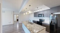 This single-floor residence offers a thoughtfully designed layout across two bedrooms and two bathrooms. The open-concept kitchen and living area serves as the heart of the home, anchored by a large granite-topped island with a double-basin sink and elegant pendant lighting. Dark-toned cabinetry with a classic white subway tile backsplash complements the full suite of black appliances, including a side-by-side refrigerator with ice and water dispenser, an electric range, and a built-in microwave. Wood-look flooring flows consistently throughout the entire space, lending warmth and visual cohesion.

The primary bedroom features a ceiling fan, a natural light source, and direct access to an en-suite bathroom. The en-suite is finished with dark vanity cabinetry, a white countertop, and a sliding glass-door walk-in shower. A dedicated walk-in closet with multiple hanging rods and shelving provides generous storage. The second bedroom also includes a ceiling fan and sliding glass door access to an outdoor area. The second bathroom mirrors the modern finishes of the first, featuring a tub-shower combination. A sliding-door closet serves the secondary bedroom. The hallway connects all rooms efficiently, completing a functional and contemporary floor plan.