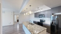 This single-floor residence offers a thoughtfully designed layout across two bedrooms and two bathrooms. The open-concept kitchen and living area serves as the heart of the home, anchored by a large granite-topped island with a double-basin sink and elegant pendant lighting. Dark-toned cabinetry with a classic white subway tile backsplash complements the full suite of black appliances, including a side-by-side refrigerator with ice and water dispenser, an electric range, and a built-in microwave. Wood-look flooring flows consistently throughout the entire space, lending warmth and visual cohesion.

The primary bedroom features a ceiling fan, a natural light source, and direct access to an en-suite bathroom. The en-suite is finished with dark vanity cabinetry, a white countertop, and a sliding glass-door walk-in shower. A dedicated walk-in closet with multiple hanging rods and shelving provides generous storage. The second bedroom also includes a ceiling fan and sliding glass door access to an outdoor area. The second bathroom mirrors the modern finishes of the first, featuring a tub-shower combination. A sliding-door closet serves the secondary bedroom. The hallway connects all rooms efficiently, completing a functional and contemporary floor plan.