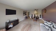 This single-floor residence offers a thoughtfully designed layout that balances comfort and functionality. The open living and dining area is generously sized, featuring plush carpeting, neutral-toned walls with an accent purple wall, and a sliding glass door that fills the space with natural light and provides outdoor views. A ceiling fan adds a practical touch to the dining area, which comfortably accommodates a round glass dining table.

The kitchen is well-equipped with rich dark-stained cabinetry, granite countertops, a classic subway tile backsplash, and stainless steel appliances including a gas range and built-in microwave — a functional and stylish space for cooking.

The bedrooms are carpeted and restful in atmosphere. The primary bedroom features a calming blue-grey accent wall, a built-in niche display shelf, and a window with blinds allowing natural light. A second bedroom maintains a soft, neutral palette with warm lighting, creating a serene and welcoming retreat.

The bathroom presents a dark wood vanity with a white countertop and a large wall mirror, paired with a separate shower-tub combination. Clean lines and light tones give the space a crisp, practical feel.

Overall, this residence offers a cohesive and comfortable living environment with a warm, livable ambiance throughout.