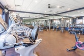 Located at 1420 Campbell St in Rahway, NJ, this fitness center at Metro Rahway is a thoughtfully designed, single-floor facility built to support a comprehensive workout experience. The space features a bold navy and neutral color scheme, with a drop-tile ceiling outfitted with recessed lighting and ceiling fans that maintain a comfortable, well-lit environment throughout.

Large windows along multiple walls flood the gym with natural light and offer views of the surrounding streetscape, creating an open and energizing atmosphere. Full-length mirrors are strategically positioned across the walls, visually expanding the space while allowing members to monitor their form during exercise.

The cardio section is well-stocked with treadmills, elliptical trainers, stationary bikes, and other aerobic machines arranged to maximize floor efficiency. The strength training area features a complete dumbbell rack spanning a wide weight range, medicine balls, stability balls, and multiple cable and cable-crossover machines suited for a variety of resistance exercises. Dedicated zones provide ample open floor space for stretching, functional training, and group fitness activities.

Durable rubber flooring covers the entire facility, providing cushioning and traction across all workout areas. A wall-mounted flat-screen television is positioned for visibility from the cardio zone. The overall layout is organized and spacious, offering residents a professional-grade fitness experience in a clean, modern setting.