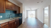 This single-floor unit is designed with a practical, open layout that connects the kitchen and living areas seamlessly. The kitchen is well-appointed with rich, dark wood cabinetry, granite countertops, and a striking blue-toned subway tile backsplash. Black and stainless steel appliances, including a range, microwave, refrigerator, and dishwasher, are neatly integrated. Wood-style plank flooring runs throughout the kitchen and living areas, adding warmth and cohesion to the space.

The living area is bright and open, benefiting from natural light that filters through a large sliding glass door fitted with vertical blinds. The door leads to a private balcony offering views of the surrounding neighborhood. A ceiling fan overhead provides both functionality and a finishing touch to the room.

The bedroom is comfortably sized, featuring plush wall-to-wall carpeting and a ceiling fan. A window provides natural light and outward views, contributing to a calm, airy atmosphere.

The bathroom features consistent wood-style flooring, a granite-topped vanity with dark wood cabinetry, and a full tub and shower combination with clean white surround. Recessed lighting throughout the unit enhances visibility and adds a polished, modern feel to the overall interior.