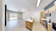This well-appointed single-story residence offers a clean, modern aesthetic throughout its thoughtfully designed floor plan. The open-concept living and kitchen area serves as the heart of the home, featuring large-format light tile flooring that flows seamlessly from room to room. The kitchen is a standout, centered around a sizeable island with a white quartz countertop, an undermount sink with a matte black faucet, and warm natural wood cabinetry that extends to the ceiling. Stainless steel appliances, including a refrigerator with ice maker, electric range, and microwave, are complemented by a white subway tile backsplash. The living area benefits from a modern globe chandelier and a ceiling fan, with sliding glass doors that invite natural light and provide outdoor access. The bedroom is a comfortable, light-filled retreat with a ceiling fan and a window with exterior views. It connects to a well-organized walk-in closet with built-in shelving and dual hanging rods. The bathroom is elegantly finished with bold geometric patterned floor tile, a wood-toned vanity with a white countertop, matte black fixtures, a large mirror with globe lighting, and a frameless glass walk-in shower.