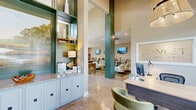 The Comet Scotts Hill leasing office at 9051 Seneca Dr in Wilmington, NC, is a thoughtfully designed single-floor community space that offers a warm and polished environment for residents and prospective tenants alike. The interior is defined by soaring ceilings, polished concrete floors, and a cohesive coastal-inspired color palette of sage green, warm beige, and natural wood tones throughout.

Guests are welcomed into an inviting reception area anchored by a built-in display cabinet with open shelving, granite countertops, and coastal artwork — a hallmark feature of the space's refined aesthetic. Tall, shiplap-clad green columns create visual structure across the open floor plan. A dedicated leasing office, framed by large windows that flood the space with natural light, provides a private setting for consultations, complete with a sleek desk and plush seating.

The expansive main area transitions seamlessly into a fully equipped kitchen featuring granite countertops, a large island with a geometric tile backsplash, stainless steel appliances, and pendant lighting — ideal for community gatherings. Adjacent to the kitchen is a comfortable lounge furnished with patterned seating and wall-mounted TVs. A separate meeting room with coastal artwork and cane-back chairs rounds out the layout. Large glass doors at the rear open directly to an outdoor pool area, enhancing the connection between indoor and outdoor amenities.