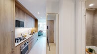 Located at 354 N Union Ave in Chicago's Fulton River District, this single-floor unit showcases a contemporary design with a cohesive warm-toned aesthetic throughout. Light wood finishes, recessed lighting, and light-toned flooring create a bright, airy atmosphere from entry to living space.

The galley-style kitchen is well-equipped with stainless steel appliances, including a gas cooktop, wall oven, and built-in microwave. Granite countertops complement the light wood cabinetry that extends floor to ceiling, maximizing storage. A full-length gold-framed mirror near the entry enhances the sense of space.

The living area is defined by dramatic floor-to-ceiling windows and sliding glass doors that open to a balcony, offering expansive views of the Chicago skyline. Natural light floods the space, creating a striking connection between the interior and the city beyond.

The bedroom features textured accent wall coverings and large windows that continue the city view experience. Two bathrooms serve the unit—one with a glass-enclosed walk-in shower, wood vanity, and open shelving, and a second full bath with a shower-tub combination, both finished with large-format tile flooring and warm wood cabinetry.