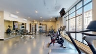 Located at 70 Park East Drive in Winnipeg, this fitness facility offers a well-appointed exercise room designed to support a comprehensive workout experience. The space is thoughtfully laid out across a single floor, providing generous room for a wide variety of training activities.

The exercise room features a durable speckled rubber flooring throughout, ideal for high-impact activity and equipment use. Large floor-to-ceiling windows along one wall flood the space with abundant natural light while offering views of the surrounding neighbourhood. Full-length wall mirrors are strategically placed to maximize the sense of openness and allow users to monitor their form.

The facility is well-stocked with a diverse selection of equipment. Cardio options include multiple treadmills, Peloton spin bikes, and a stair climber. Strength training is supported by a cable machine, a dumbbell rack with a full range of weights, an adjustable bench, and a dedicated medicine ball and kettlebell station. A flat-screen television is mounted from the ceiling for entertainment during workouts.

Climate control is provided by wall-mounted air conditioning units, ensuring a comfortable environment year-round. Recessed ceiling lighting supplements the natural light for even illumination throughout the space. The clean, neutral colour palette and modern finishes contribute to a professional and motivating atmosphere suitable for all fitness levels.