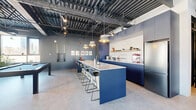 Located at 3555 Saint-Antoine O in Montreal, this single-floor amenity space offers a generously sized, thoughtfully designed environment that blends industrial architecture with modern, vibrant interiors. The exposed steel ceiling structure, complete with visible ductwork and track lighting, runs throughout, lending the space a loft-like character with impressive vertical volume.

The fitness area is well-appointed, featuring rubber tile flooring, large floor-to-ceiling windows that flood the space with natural light, and an extensive selection of equipment including treadmills, stationary bikes, weight benches, dumbbells, resistance machines, and stability balls. Full-length mirrors expand the sense of space and support workouts effectively. A glass partition wall elegantly separates the gym from the rest of the amenity floor.

The social and lounge area is equally striking, anchored by a bold navy-blue kitchen island with bar seating, navy cabinetry, open shelving, and pendant lighting. A pool table, lounge seating with a fireplace, and built-in bookshelves create a relaxed yet sophisticated gathering atmosphere. A separate seating nook with large windows and colorful accent chairs provides a bright, casual retreat. A gallery-style corridor with curated artwork connects the various zones, completing this dynamic and well-rounded amenity space.