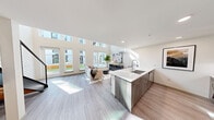 Located at 4906 25th Ave NE in Seattle's University District, this contemporary two-story residence showcases a thoughtfully designed open-concept layout with impressive double-height ceilings that flood the main living area with natural light. Floor-to-ceiling windows and clerestory glazing frame views of the surrounding courtyard and greenery, creating a bright and airy atmosphere throughout.

The main level centers on a sleek, modern kitchen equipped with stainless steel appliances, dark wood cabinetry, a white quartz waterfall island with an undermount sink, and a subway tile backsplash. The island flows seamlessly into the open dining and living area, where light wood-tone flooring and expansive windows contribute to a clean, contemporary aesthetic. A half bath on the main level adds everyday convenience.

A staircase with a modern cable railing leads to the upper loft level, which houses the bedroom suite. The bedroom features a walk-in closet and is served by a full bathroom with a wide quartz vanity and an in-unit stacked washer and dryer. The upper level also includes an open loft area with windows overlooking the surrounding neighborhood, ideal as a sitting area or home office. Throughout, the interiors reflect a consistent modern design language with neutral tones, recessed lighting, and high-quality finishes.