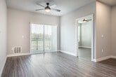 This single-floor unit showcases a contemporary design with consistent wood-look flooring and a neutral grey-and-white color palette throughout. The open-concept kitchen serves as the centerpiece, featuring rich dark-stained cabinetry, granite countertops, and a full suite of stainless steel appliances including a French door refrigerator and electric range. A substantial kitchen island with an undermount sink is illuminated by three gold-accented pendant lights, creating a functional and stylish focal point that opens directly to the living area.

The living space benefits from a sliding glass door fitted with vertical blinds, offering outdoor views and ample natural light. The bedrooms are well-proportioned, each with wood-look flooring, neutral walls, and windows that invite natural light. One bedroom includes a ceiling fan and dual windows, while another features a closet and convenient access to adjacent rooms.

The bathrooms are finished with granite-topped vanities, dark-framed mirrors, and dark hardware accents. The primary bathroom includes a walk-in roll-in shower with grab bars and a handheld showerhead, reflecting an accessibility-conscious design. Recessed lighting and thoughtful finishes contribute to the unit's clean, modern ambiance throughout.