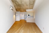 Located at 2600 Cavendish Boulevard in Montréal, this thoughtfully designed unit blends modern finishes with industrial character. The open-concept kitchen and living area forms the heart of the space, where warm light wood flooring runs seamlessly underfoot and a striking exposed concrete ceiling adds a raw, loft-inspired aesthetic. A wall-mounted mini-split unit ensures year-round climate comfort.

The kitchen is well-appointed with white upper cabinetry, a sleek glass backsplash, stainless steel appliances including a built-in microwave, electric range, and refrigerator, and a functional island featuring a wood-toned base, white quartz countertop, and undermount sink — ideal for both cooking and casual dining. Track lighting overhead illuminates the workspace efficiently.

The living area benefits from a large black-framed glass door that opens to an outdoor balcony, flooding the interior with natural light and offering views of the surrounding Montréal neighbourhood. A pendant light adds a subtle design touch to the open space.

The bathroom is clean and minimal, finished entirely in white large-format tile, with a full bathtub and shower combination. A dedicated closet provides practical storage. Throughout the unit, the contrast of crisp white walls against the textured concrete ceiling creates a refined yet contemporary ambiance.