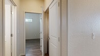 This single-story, 2-bedroom, 2-bathroom home offers a thoughtfully designed layout with a clean, modern aesthetic. The open-concept kitchen is a standout feature, showcasing rich dark wood cabinetry, white quartz-style countertops, a peninsula breakfast bar, and a full suite of stainless steel appliances including a refrigerator with ice maker, range, microwave, and dishwasher. A window above the sink allows natural light to fill the space. The main living area is bright and airy, featuring wood-look laminate flooring, a ceiling fan, and multiple windows with horizontal blinds that invite natural light while maintaining privacy. The hallway connects the bedrooms and bathrooms, finished with textured walls and consistent wood-look flooring throughout. The primary bedroom is generously sized, offering ample room for furnishings, with windows providing natural light. The second bedroom is equally well-proportioned with its own window. Both bathrooms are finished with dark wood vanities, light countertops, large mirrors, and shower enclosures. A dedicated closet and hallway complete the functional floor plan, making this a practical and comfortable single-level home.