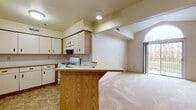 This third-floor, 1-bedroom, 1-bathroom unit is thoughtfully designed to maximize both function and comfort. The open-concept layout connects the kitchen and living area seamlessly, creating a spacious, airy feel throughout.

The kitchen features cream-colored cabinetry with warm oak accents, ample upper and lower storage, light countertops, and a gas range with a built-in overhead exhaust. A freestanding oak peninsula provides additional prep space and serves as a natural divider between the kitchen and living areas. Tile flooring anchors the kitchen zone, while plush wall-to-wall carpeting extends throughout the living area and bedroom.

The living area is bright and open, highlighted by a striking arched window that fills the space with natural light and provides access to an outdoor balcony. Vaulted ceilings add an impressive sense of vertical space, contributing to the unit's open and welcoming ambiance.

The bedroom is a generously sized, quiet retreat with soft carpeting, neutral walls, and structural beam detailing along the ceiling that adds architectural character.

The bathroom is clean and functional, finished with stone-look tile flooring and equipped with standard fixtures. A bi-fold door entry adds space efficiency to the layout.

Overall, this unit offers a practical and comfortable living environment with consistent neutral tones and classic finishes throughout.