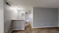 This single-floor, 2-bedroom, 2-bathroom home offers a practical and comfortable layout designed for efficient living. The combined living and dining area greets you upon entry, featuring wood-look flooring, neutral gray walls, a textured ceiling, and a pendant light fixture above the dining space. A kitchen bar peninsula separates the kitchen from the main living area, while white cabinetry and a stainless steel refrigerator equip the kitchen with everyday functionality. The open-concept design allows the living and dining spaces to flow naturally into one another, creating a cohesive and inviting atmosphere. The primary bedroom is generously sized, featuring plush carpet, dual windows with blinds that invite natural light, and a ceiling fan with a light kit. The second bedroom also offers carpeted flooring, a ceiling fan, and a window overlooking the outdoors. Both bathrooms are finished with wood-look flooring, white vanities with light countertops, tall storage cabinetry, and chrome fixtures. A connecting hallway links the bedrooms and bathrooms, with four closets distributed throughout the home providing substantial storage. The consistent gray color palette and clean white trim throughout create a cohesive, move-in-ready aesthetic.