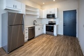 Located at 2004 City Vista Way in Knoxville, Tennessee, this contemporary single-floor unit showcases a clean, modern aesthetic throughout. The open-concept living and kitchen area is anchored by warm wood-tone vinyl flooring that flows seamlessly from room to room. Large floor-to-ceiling windows and a sliding glass door flood the living space with abundant natural light while providing direct access to a private balcony overlooking the surrounding cityscape.

The kitchen is thoughtfully designed with crisp white cabinetry, open shelving, light-toned countertops, and a full suite of stainless steel appliances including a refrigerator, dishwasher, electric range, and over-the-range microwave. A matte black faucet and sink add a stylish contrast to the bright cabinetry. Track lighting with black fixtures runs throughout the living and kitchen areas, offering both function and a modern industrial touch.

The bedroom is generously sized, featuring its own access to the balcony via a large sliding glass door, an additional window for cross-ventilation, and continued wood-tone flooring. The bathroom is finished with white cabinetry, a dual-sink vanity with quartz-style countertop, matte black fixtures, a walk-in glass-door shower, and warm wood flooring. A bold teal entry door provides a striking accent at the unit's entrance, completing the modern, design-forward character of the space.