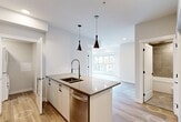 Located at 8450 106A Avenue NW in Edmonton, Alberta, this modern 3-bedroom, 2-bathroom unit offers a thoughtfully designed single-floor layout with contemporary finishes throughout. Light-toned hardwood flooring flows seamlessly across all living areas, complementing the clean, neutral palette of the interior.

The open-concept kitchen and living area serves as the heart of the unit, featuring a central island with a quartz countertop, undermount sink, and sleek pendant lighting. White cabinetry, a navy-tiled backsplash, and stainless steel appliances — including a range, microwave, and refrigerator — complete the well-appointed kitchen.

Three bedrooms offer comfortable accommodations, each with large floor-to-ceiling windows that frame views of the surrounding Edmonton neighbourhood and fill the rooms with natural light. One bedroom includes a closet with built-in shelving. The two bathrooms are finished with large-format grey tile, featuring a glass-enclosed shower in one and a soaker tub with tiled surround in the other, both accented with black hardware details. A dedicated laundry area houses a stacked Whirlpool washer and dryer for added convenience. The overall ambiance is bright, clean, and modern.