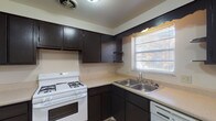 Located at 4550 Hilton Ave in Columbus, Ohio, this single-floor unit offers a practical and straightforward layout suited for everyday living. The kitchen is well-equipped with dark espresso-toned cabinetry providing ample upper and lower storage, light-colored countertops, a white gas range, a double stainless steel sink, and a dishwasher. A window above the sink allows natural light to brighten the space, which features durable tile-style flooring throughout. The living area is generously sized, finished with wall-to-wall carpet, and connects openly to the kitchen. Large sliding glass doors dressed with vertical blinds allow additional natural light into the living space. The bedrooms are comfortably proportioned, each featuring soft carpeting and multiple windows that bring in natural light from multiple directions. The full bathroom includes a tub and shower combination with a distinctive teal tub, a white vanity with sink, a toilet, hardwood-style flooring, and a window for ventilation. The overall layout, as seen in the dollhouse view, is compact yet efficient, with clearly defined living, sleeping, and kitchen zones all on a single level.