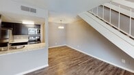 This two-story unit in Hedwig Village, Texas, offers a well-designed layout with thoughtful finishes throughout. The main level features durable wood-look flooring that flows through the open living and dining areas. A staircase with white railings connects the floors, while a pendant light fixture highlights the dining space. The kitchen opens to the living area via a pass-through counter finished with light granite-style countertops. Dark espresso cabinetry lines both sides of the galley-style kitchen, complemented by stainless steel appliances, including a refrigerator, range, and microwave. A stainless steel sink is integrated into the counter for added convenience.

The upper level houses the spacious bedroom, finished with plush carpet and neutral gray walls. A ceiling fan overhead, a window with blinds providing natural light, and a walk-in closet make this a comfortable retreat. The bathroom is equipped with a dark vanity topped with light stone-look countertops, overhead cabinetry for storage, and wood-look flooring. Textured ceilings are present throughout, and ceiling fans in both the living area and bedroom enhance comfort year-round.