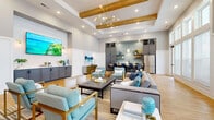 Located at 5905 Campbellton Rd SW in South Fulton, Georgia, this single-story community clubhouse delivers a polished, contemporary atmosphere defined by thoughtful design and high-quality finishes throughout. The open-concept main area is anchored by soaring ceilings adorned with warm wood beams and a coffered tray detail, with a striking sputnik-style brass chandelier serving as a central focal point. Light hardwood flooring flows continuously throughout the space, complementing the neutral gray and white color palette accented by aqua and navy blue furnishings.

The main lounge features a generously scaled seating arrangement with plush sofas and gold-framed accent chairs, centered around a tufted leather coffee table. A large wall-mounted flat-screen television is positioned above a bank of gray shaker-style cabinetry with white quartz countertops. An adjacent dining area showcases dark cabinetry, bar-height seating, and a decorative blue tile backsplash that adds textural interest.

A private meeting room offers an intimate round table setting with tall ceilings, wainscoting, and curated artwork. The kitchenette is equipped with a stainless steel French door refrigerator, undermount sink, quartz counters, open shelving, and the same blue tile backsplash. Floor-to-ceiling windows along one wall flood the space with abundant natural light and provide views of the surrounding exterior.