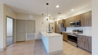 This single-floor unit showcases a modern, open-concept design centered around a well-appointed kitchen. The kitchen features a generous island with a light granite countertop, an undermount sink, and sleek pendant lighting overhead. Warm wood-toned cabinetry lines the walls, complemented by a white subway tile backsplash and a full suite of stainless steel appliances, including a refrigerator, range, and built-in microwave. Light hardwood-style flooring extends throughout the main living areas, enhancing the bright, airy ambiance created by recessed lighting.

The bedrooms are finished with plush carpeting and ceiling fans, and benefit from natural light through sliding windows with outdoor views. The primary bedroom includes direct access to an en-suite bathroom featuring a wood-front vanity with granite countertop, light tile flooring, and a glass-enclosed walk-in shower. A secondary bathroom offers a tiled tub-shower combination. A dedicated laundry room with a full-size washer and dryer adds everyday convenience. The overall design palette of neutral tones, quality finishes, and cohesive materials gives the space a clean, contemporary feel throughout.