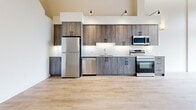 Located at 647 Goldstream Avenue in Langford, BC, this two-storey, two-bedroom, two-bathroom unit offers a well-designed layout spread across two generous floors. The main floor features a contemporary kitchen equipped with wood-toned cabinetry, a white tile backsplash, quartz countertops, and a full suite of stainless steel appliances including a refrigerator, dishwasher, electric range, and built-in microwave. Light hardwood-style flooring runs throughout the main level, creating a warm and cohesive aesthetic. A carpeted staircase connects to the upper floor, where a dramatic vaulted ceiling clad in natural wood planking adds striking architectural character. A ceiling fan and exposed structural beams contribute to the loft-like ambiance of the upper level. Both bathrooms are finished with wood-grain vanities, matte black hardware, quartz countertops, and light hardwood-style flooring. One bathroom features a sliding glass shower enclosure, while the other includes a bathtub. The bedrooms are bright and clean, with one offering a serene, minimal aesthetic highlighted by warm wall sconce lighting. Throughout the unit, crisp white walls, black hardware accents, and quality finishes create a cohesive modern style.