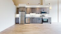 Located at 647 Goldstream Avenue in Langford, BC, this two-storey, two-bedroom, two-bathroom unit offers a well-designed layout spread across two generous floors. The main floor features a contemporary kitchen equipped with wood-toned cabinetry, a white tile backsplash, quartz countertops, and a full suite of stainless steel appliances including a refrigerator, dishwasher, electric range, and built-in microwave. Light hardwood-style flooring runs throughout the main level, creating a warm and cohesive aesthetic. A carpeted staircase connects to the upper floor, where a dramatic vaulted ceiling clad in natural wood planking adds striking architectural character. A ceiling fan and exposed structural beams contribute to the loft-like ambiance of the upper level. Both bathrooms are finished with wood-grain vanities, matte black hardware, quartz countertops, and light hardwood-style flooring. One bathroom features a sliding glass shower enclosure, while the other includes a bathtub. The bedrooms are bright and clean, with one offering a serene, minimal aesthetic highlighted by warm wall sconce lighting. Throughout the unit, crisp white walls, black hardware accents, and quality finishes create a cohesive modern style.