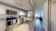 Located at 1101 Iroquois Ave in Naperville, IL, this well-appointed single-floor residence offers a thoughtfully designed layout with modern finishes throughout. The open-concept kitchen is a standout feature, showcasing white shaker cabinetry, subway tile backsplash, granite-style countertops, stainless steel appliances including a range, microwave, and dishwasher, and a peninsula with bar seating that connects seamlessly to the dining and living areas. Wood-style flooring runs throughout the main living spaces, lending warmth and continuity to the open floor plan. The living area is highlighted by a striking bay window configuration that floods the room with natural light and offers pleasant views of the surrounding greenery. A dedicated dining nook sits adjacent to the kitchen pass-through, ideal for casual meals. The bedroom is a comfortable retreat featuring plush carpeting, multiple windows with outdoor views, and ample room for furnishings. The bathroom is equipped with both a soaking tub and a separate glass-enclosed shower, adding a spa-like quality. A dedicated in-unit laundry area with full-size washer and dryer hookups adds everyday convenience. Textured ceilings and track lighting complete the interior aesthetic, making this a functional and inviting space.