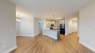 This single-floor residence presents a thoughtfully designed open-concept layout that seamlessly connects the main living areas. The kitchen serves as a central focal point, featuring a granite-topped peninsula island with an undermount sink, gray shaker-style cabinetry, and black appliances including a refrigerator, range, and built-in microwave. Pendant lighting illuminates the island, complementing the under-cabinet and recessed lighting throughout. Light hardwood-style flooring extends across the kitchen and main living areas, contributing to a bright, cohesive aesthetic.

The spacious living area benefits from a bank of windows that invite natural light and offer exterior views, enhanced by a ceiling fan overhead. A hallway connects the private areas of the residence, lined with white panel doors and recessed lighting. The bedroom features plush carpeting, a ceiling fan, and a generously sized window. A walk-in closet with wire shelving provides ample storage. The bathroom is well-appointed with a gray vanity topped with granite, a framed mirror, overhead cabinetry, and a glass-enclosed shower. Consistent neutral tones and clean finishes create a modern, move-in-ready atmosphere throughout.