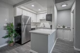 Located at 3610 Banbury Dr in Riverside, California, this single-floor residence offers a clean, modern aesthetic with a cohesive neutral color palette of soft gray tones and crisp white trim throughout. Light-toned laminate wood flooring extends seamlessly across the living areas and bedrooms, lending a sense of continuity and warmth.

The open living area is spacious and bright, anchored by a ceiling fan and direct sightlines to the kitchen, creating an inviting, connected layout. The kitchen features white shaker-style cabinetry, light countertops, a stainless steel refrigerator, and a peninsula that provides additional prep space and separates the kitchen from the main living area. Recessed lighting above enhances the kitchen's clean, functional design.

Multiple bedrooms offer comfortable proportions, each finished with the same laminate flooring and soft gray walls. Windows in the bedrooms frame views of the surrounding palm-lined outdoor environment, filling the rooms with natural light. One bedroom includes a sliding glass door providing access to an outdoor area.

The two bathrooms are finished in a bright, neutral style, each featuring white vanity cabinetry, light countertops, framed mirrors, and laminate flooring. One bathroom includes a shower-tub combination, while the other serves as a half or utility bath. Textured ceilings are present throughout the home, adding a classic residential character.