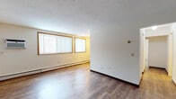 This single-floor unit offers a practical and comfortable layout designed for everyday living. The open living area is finished with durable hardwood-style flooring, neutral-toned walls, and a textured ceiling, creating a clean and bright atmosphere. Large windows fitted with vertical blinds allow generous natural light to fill the space, while baseboard heating ensures year-round comfort. A wall-mounted air conditioning unit provides additional climate control in the living area.

The kitchen is well-appointed with warm oak cabinetry, granite-style countertops, and stainless steel appliances including a range and microwave. Hardwood-style flooring continues throughout, and a ceiling fan with light fixture adds both function and airflow. A hallway connects the main living areas to the private spaces, with a closet conveniently accessible along the corridor.

The bedrooms feature plush carpeting, ceiling fans, and corner windows with vertical blinds that invite natural light from multiple angles. Baseboard heating runs along the perimeter of each room, ensuring consistent warmth. The full bathroom is finished with classic white subway tile surrounding the tub and shower, complemented by a mosaic tile floor, a warm oak vanity with medicine cabinet mirror, and clean white fixtures throughout. The overall ambiance is functional, well-maintained, and move-in ready.