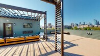 Located at 416 Vine St in Philadelphia's historic Old City neighborhood, this generously sized rooftop deck offers an exceptional outdoor living experience with panoramic views of the Philadelphia skyline. The deck is thoughtfully designed with composite wood decking in complementary tones, creating distinct zones for lounging, dining, and entertaining across its expansive footprint.

Multiple wood-framed pergolas with slatted side screens define gathering areas while allowing natural light to filter through, and string lights add ambiance for evening use. A comfortable lounge zone features low-profile sectional seating with plush cushions, complemented by bean bag chairs and a wall-mounted flat-screen TV with a built-in linear fireplace beneath it. A dedicated fire pit area is set within a gravel surround, flanked by Adirondack chairs, creating an intimate retreat. The rooftop also includes a built-in outdoor kitchen and bar area, raised planter beds with greenery, and a built-in bench with city views.

The sage-green horizontal siding of the surrounding structure ties the design together cohesively, while open sightlines ensure unobstructed views of Philadelphia's skyline in multiple directions. This rooftop is a well-appointed outdoor space ideal for both relaxation and entertainment.