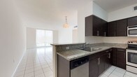 Unit 603 is a well-appointed single-floor residence characterized by a clean, contemporary design carried consistently throughout its spaces. The kitchen is a standout feature, equipped with dark espresso cabinetry, granite countertops, and a full suite of stainless steel appliances, including a refrigerator, range, and built-in microwave. A peninsula with a stainless steel sink connects the kitchen to the living and dining area, creating an open, functional flow. The living area is generously proportioned, bathed in natural light through floor-to-ceiling sliding glass doors that open to a balcony with open city views. White large-format tile flooring extends throughout the entire unit, lending a bright and cohesive aesthetic. The bedrooms are comfortably sized, each featuring windows that frame urban skyline views and allow ample natural light. Two bathrooms serve the unit; one includes a soaking tub with a tiled surround, while the other features a glass-enclosed walk-in shower. Both bathrooms are finished with granite-topped white vanities, large mirrors, and white tile flooring, maintaining the unit's consistent, modern palette throughout.