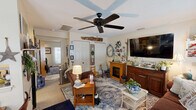 Located at 194 N Elm St in Manchester, Connecticut, this cozy one-bedroom, one-bathroom residence offers a warm and inviting single-floor layout. The living room serves as the heart of the home, featuring a ceiling fan, a textured ceiling, a decorative wood beam accent, and an electric fireplace framed by a wood mantel. Multiple windows dressed with floral curtains allow natural light to brighten the space, while a large wall-mounted TV and a classic area rug add comfort and character. A dedicated dining area is visible nearby, creating a natural flow for everyday living. The kitchen is efficiently laid out in a U-shape, outfitted with warm honey-toned wood cabinetry, a coil-burner electric range, dishwasher, and full-size refrigerator, all set atop light vinyl flooring. The bedroom is a serene retreat, complete with its own ceiling fan, carpeted flooring, a private exterior door, and a window with natural light. The bathroom features charming botanical-print wallpaper and a ruffled white shower curtain, adding a touch of whimsy. A closet provides additional storage. Throughout the home, a cozy, cottage-inspired aesthetic ties each room together cohesively.
