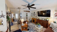 Located at 194 N Elm St in Manchester, Connecticut, this cozy one-bedroom, one-bathroom residence offers a warm and inviting single-floor layout. The living room serves as the heart of the home, featuring a ceiling fan, a textured ceiling, a decorative wood beam accent, and an electric fireplace framed by a wood mantel. Multiple windows dressed with floral curtains allow natural light to brighten the space, while a large wall-mounted TV and a classic area rug add comfort and character. A dedicated dining area is visible nearby, creating a natural flow for everyday living. The kitchen is efficiently laid out in a U-shape, outfitted with warm honey-toned wood cabinetry, a coil-burner electric range, dishwasher, and full-size refrigerator, all set atop light vinyl flooring. The bedroom is a serene retreat, complete with its own ceiling fan, carpeted flooring, a private exterior door, and a window with natural light. The bathroom features charming botanical-print wallpaper and a ruffled white shower curtain, adding a touch of whimsy. A closet provides additional storage. Throughout the home, a cozy, cottage-inspired aesthetic ties each room together cohesively.