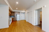 Located at 2065 S River Pkwy in Portland, Oregon, this well-designed one-bedroom, one-bathroom residence offers a practical and comfortable layout. The open-plan kitchen and living area forms the heart of the home, featuring warm hardwood-style flooring that extends throughout the main space. The kitchen is outfitted with rich wood cabinetry, light countertops, a full suite of white appliances including a range, dishwasher, and refrigerator, and a built-in range hood — all designed for functional everyday living. Recessed lighting illuminates the combined kitchen and living area, which benefits from a large window fitted with vertical blinds that allows generous natural light to fill the room. The bedroom is a well-proportioned private retreat, carpeted for comfort and featuring its own large window that brings in additional natural light. A dedicated walk-in closet off the bedroom provides ample storage with wire shelving and hanging rails. The bathroom features a wood-toned vanity with light stone-effect countertops, an undermount sink, and mirrored medicine cabinets. Clean white walls and consistent finishes throughout give the space a cohesive, modern feel suited to urban living in Portland.