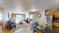 Located at 1301 31st Ave SW in Minot, North Dakota, this single-floor residence offers a thoughtfully designed open-concept layout that seamlessly connects the kitchen, dining, and living areas. The kitchen is a standout feature, showcasing warm oak cabinetry, granite countertops, a mosaic tile backsplash, stainless steel appliances, and a central island with bar seating — ideal for both everyday meals and entertaining. Wood-look flooring extends throughout the main living areas, adding a clean, contemporary feel. The dining area accommodates a round table with bar-height seating, while the living room offers generous space filled with natural light from a sliding glass door that leads to a private balcony. Multiple bedrooms are carpeted for comfort, each equipped with a ceiling fan, natural light from large windows, and ample closet space. The bathroom features a granite-topped vanity with oak cabinetry, a tub-shower combination, a large mirror, and wood-look flooring that complements the rest of the unit. A hallway connecting the bedrooms and bathroom provides additional storage. The overall ambiance is warm and functional, with neutral tones and consistent finishes creating a cohesive living environment throughout the home.