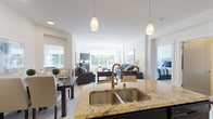 This single-floor residence is designed around an open-concept layout that seamlessly connects the kitchen, dining, and living areas, creating a bright and cohesive living environment. The kitchen serves as a central hub, anchored by a large island with warm granite countertops and a double undermount stainless steel sink. Pendant lighting hangs above the island, while rich dark-wood cabinetry lines the walls alongside stainless steel appliances, including a range, microwave, and refrigerator. Light hardwood-style flooring runs throughout the kitchen and laundry areas.

The open living space flows naturally from the kitchen, featuring plush carpeting, large windows that invite abundant natural light, and access to an outdoor area. The dining zone sits comfortably adjacent, offering a defined yet connected space for entertaining.

The bedrooms are generously proportioned, each with soft carpeting, wide windows framing outdoor greenery, and neutral walls that create a calm atmosphere. The bathroom features a elongated vanity with dark wood cabinetry, a large mirror, tile flooring, and a separate water closet for added privacy.

A dedicated in-unit laundry room houses a full-size washer and dryer with overhead cabinetry, adding everyday convenience to this well-appointed residence.