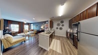 This single-story residence is thoughtfully designed with an open-concept layout that seamlessly connects the kitchen, dining, and living areas. The kitchen is equipped with stainless steel appliances, including a refrigerator, microwave, and range, complemented by rich dark-wood cabinetry and granite countertops. A peninsula with an undermount sink extends into the main living space, making it ideal for both meal preparation and casual dining. Wood-style flooring runs throughout the common areas, adding warmth and continuity.

The living room features a bold dark accent wall, a ceiling fan, and natural light from surrounding windows. Two bedrooms each carry distinct character: one showcases a dark accent wall with neutral carpet and an en-suite bathroom that includes a walk-in closet and glass-enclosed shower, while the second bedroom features a warm terracotta accent wall, carpeted floors, and ample natural light. Both rooms include ceiling fans.

The bathrooms are finished with granite-topped vanities, dark wood cabinetry, and wood-style flooring. A full guest bathroom with a large mirror and bright vanity lighting serves the secondary bedroom. Overall, the space presents a cohesive, contemporary aesthetic with bold color choices and quality finishes throughout.