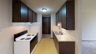 This single-floor residential unit offers a functional and straightforward layout across several well-defined living spaces. The living room is generously proportioned, featuring wall-to-wall carpet, neutral-toned walls, a textured ceiling, and a ceiling fan with light fixture. A large sliding glass door with vertical blinds fills the room with natural light and provides an outdoor view, creating an open, airy feel.

The galley-style kitchen runs parallel along both walls and is equipped with dark wood cabinetry above and below the countertops, a double-basin sink, a coil-burner electric range, a refrigerator, and a range hood. The kitchen features durable vinyl tile flooring and offers ample storage through its full run of upper and lower cabinets. A closet is accessible directly from the kitchen area.

The bedroom is a well-sized, carpeted room with neutral walls, a textured ceiling, a flush-mount light fixture, and a window fitted with horizontal blinds that allows natural light while maintaining privacy. A baseboard heater runs along the exterior wall, providing direct warmth.

The bathroom includes a full-sized tub and shower combination with white tile surround, a toilet, vanity with countertop, and patterned vinyl tile flooring. A towel bar and toilet paper holder complete the functional fixtures in this clean, simply appointed space.