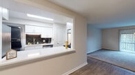 This single-floor residence offers a thoughtfully arranged layout that balances functionality with a clean, modern aesthetic. The heart of the home is the kitchen, which features crisp white cabinetry with brushed hardware, a bold dark subway tile backsplash, white countertops, and stainless steel appliances including a dishwasher and electric range. A pass-through window with a countertop bar connects the kitchen to the adjacent living area, creating an open, communicative flow between spaces. The living area is finished with warm wood-look flooring, while neutral-toned walls throughout lend a bright, airy feel. The two bedrooms are carpeted for comfort, each featuring neutral walls and window blinds that allow natural light to filter in, creating a calm and restful atmosphere. Closet access is provided in at least one bedroom via a bifold door. The bathroom is finished with white shiplap-style wall paneling, warm tile flooring, a full tub-and-shower combination, and a white vanity with ample storage. A second bathroom features similar clean finishes. The overall design is cohesive and understated, with consistent trim work and neutral tones throughout that provide a versatile backdrop for any style of furnishing.