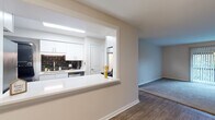 This single-floor residence offers a thoughtfully arranged layout that balances functionality with a clean, modern aesthetic. The heart of the home is the kitchen, which features crisp white cabinetry with brushed hardware, a bold dark subway tile backsplash, white countertops, and stainless steel appliances including a dishwasher and electric range. A pass-through window with a countertop bar connects the kitchen to the adjacent living area, creating an open, communicative flow between spaces. The living area is finished with warm wood-look flooring, while neutral-toned walls throughout lend a bright, airy feel. The two bedrooms are carpeted for comfort, each featuring neutral walls and window blinds that allow natural light to filter in, creating a calm and restful atmosphere. Closet access is provided in at least one bedroom via a bifold door. The bathroom is finished with white shiplap-style wall paneling, warm tile flooring, a full tub-and-shower combination, and a white vanity with ample storage. A second bathroom features similar clean finishes. The overall design is cohesive and understated, with consistent trim work and neutral tones throughout that provide a versatile backdrop for any style of furnishing.