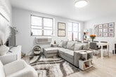 Located at 11 New St in Somerville, NJ, this single-floor residence offers a clean, modern aesthetic defined by light-toned hardwood-style flooring, crisp white walls, and an abundance of natural light streaming through multiple windows fitted with sleek horizontal blinds. The welcoming entryway opens to a thoughtfully arranged living space featuring a generous sectional sofa, a stylish media console, and layered area rugs that add warmth and texture to the bright interior. Multiple windows frame views of the surrounding neighborhood, keeping the living area feeling airy and connected to the outdoors. The adjacent dining area comfortably accommodates a full dining table and is accented by a curated gallery wall, a bookcase, and additional windows that further enhance the natural light throughout. The kitchen is well-appointed with white shaker-style cabinetry extending to the ceiling, a neutral tile backsplash, and a full suite of stainless steel appliances including a refrigerator, range, microwave, and dishwasher. The spacious bedroom provides a serene retreat with multiple windows, ample floor space for a dedicated work area and vanity, and a wall-mounted television. Throughout the residence, the consistent light palette and cohesive design create a calm, contemporary ambiance.