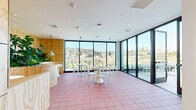 Located at 200 Mesnager St in Los Angeles, CA, this rooftop dining space offers a thoughtfully designed environment that blends indoor comfort with striking outdoor scenery. The single-floor layout features a bright, open dining area finished with distinctive terracotta-toned floor tiles that add warmth to the modern aesthetic. Floor-to-ceiling black-framed glass windows and sliding doors line the perimeter, flooding the interior with abundant natural light and framing sweeping panoramic views of the surrounding Los Angeles hillside landscape. A variety of seating arrangements — including sleek round bistro tables with white bentwood chairs and illuminated white accent stools — provide flexible dining configurations throughout the space. Pendant lights, both polished silver and aged copper in finish, hang above the tables to create intimate focal points. A built-in curved wood banquette, clad in light plywood paneling, features an integrated planter overflowing with lush tropical greenery, adding a vibrant natural element to the interior. The adjacent outdoor terrace, enclosed by a glass-railed balcony, extends the usable area and offers an al fresco dining experience with unobstructed views of the rolling hills beyond. A small service counter provides functional support for the dining area, and a clean entryway connects the interior to the outdoor terrace seamlessly.