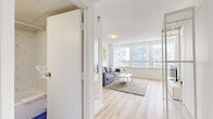 Located on Boulevard René-Lévesque Ouest in the heart of Montréal, this well-appointed one-bedroom, one-bathroom unit offers a clean and modern living experience across a single floor. Light hardwood flooring flows throughout the space, creating a warm and cohesive atmosphere.

The living room is bright and inviting, anchored by a large multi-pane window that frames city skyline views and fills the room with natural light. The open layout comfortably accommodates a seating area and entertainment setup, making it a functional and welcoming space.

The bedroom continues the minimalist aesthetic with the same light hardwood flooring, crisp white walls, and generous windows overlooking the surrounding urban landscape. The room offers a calm and restful atmosphere with ample natural light.

The kitchen is efficiently designed with white cabinetry, a tiled backsplash, and full-size appliances including a refrigerator, stove, and microwave. A butcher block-topped island on casters provides additional prep and storage space.

The bathroom features bold cobalt blue floor tiles contrasted by white diamond-patterned wall tiles, a pedestal sink, and a glass-shelf vanity mirror, adding a distinctive character to the otherwise neutral palette. A built-in closet with bi-fold doors in the living area provides practical storage. This unit offers a comfortable and stylish urban retreat in a prime Montréal location.