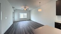 This efficiently designed 510-square-foot, one-bedroom, one-bathroom apartment offers a modern aesthetic across a single floor. The open-concept living and kitchen area is anchored by rich, dark hardwood-style flooring and crisp white walls, creating a clean, contemporary contrast. The kitchen is equipped with dark espresso cabinetry, a white subway tile backsplash, stainless steel appliances including a refrigerator and dishwasher, and a central island with a light quartz countertop and an integrated sink — ideal for both cooking and casual dining. Recessed lighting illuminates the kitchen and living area, while a pendant light and ceiling fan add functional style to the open living space, which also features a window allowing natural light to filter in. The bedroom, approximately 450 square feet, is finished with plush carpet, a ceiling fan, and a large window offering outdoor views of green space, providing a calm and comfortable retreat. The bathroom features a sleek dark vanity with light quartz countertops, a wide undermount sink, chrome fixtures, a large mirror, and tall dark cabinetry for ample storage. This unit combines modern design with practical functionality throughout.