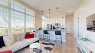 Located at 307 E 1st St in the heart of downtown Dayton, Ohio, this modern single-floor residence offers a thoughtfully designed open-concept layout with clean lines and contemporary finishes throughout. The living area is a bright, welcoming space anchored by floor-to-ceiling windows that frame views of the Dayton skyline, flooding the room with natural light and creating an airy, elevated atmosphere. Light hardwood-style flooring runs throughout the main living spaces, complementing the neutral color palette.

The kitchen is a standout feature, boasting sleek white cabinetry, dark quartz countertops, and a full suite of stainless steel appliances including a refrigerator, range, and built-in microwave. A generous island with seating for multiple bar stools serves as both a functional workspace and a casual dining area, while stylish pendant lighting adds a modern touch overhead.

The bedroom is a serene retreat, carpeted for comfort, with a large window offering natural light and city views. It is complemented by a spacious walk-in closet with extensive shelving and hanging storage. The bathroom features a floating vanity with dark countertops, a framed mirror, a glass-enclosed shower, and warm hardwood-style flooring, delivering a clean and functional design.