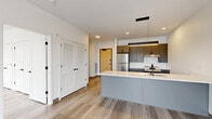 Located at 2132 Stokes Blvd in Cleveland's vibrant University Circle neighborhood, this thoughtfully designed one-bedroom, one-bathroom residence offers a modern aesthetic throughout its efficiently laid-out single floor. The open-concept living, dining, and kitchen area serves as the heart of the unit, anchored by a sleek kitchen island with a white quartz countertop, an undermount sink with a matte black faucet, and built-in microwave. Cabinetry in a contemporary gray-taupe finish pairs with stainless steel appliances, including a refrigerator and range, set against a clean white tile backsplash. Pendant lighting and recessed fixtures illuminate the space warmly. Light wood-tone flooring flows consistently throughout, complementing the bright, neutral palette. The living area extends toward a sliding glass door that opens to a balcony with open city views. The spacious bedroom features large floor-to-ceiling windows framing panoramic Cleveland skyline views, along with generous closet space across multiple built-in closets. The bathroom is finished with elegant herringbone-patterned marble-look tile flooring, a floating vanity, and matte black hardware accents. In-unit laundry adds everyday convenience to this clean, contemporary residence.