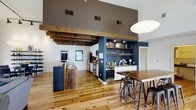 Located at 300 Blackwell St in the heart of Durham, NC, this single-floor space blends industrial character with warm, inviting design. The open-plan layout is anchored by dramatically high ceilings that amplify the sense of volume and airiness throughout. Reclaimed wood ceiling beams add rustic texture and visual depth, complementing the wide-plank hardwood floors that run the length of the space.

The fully equipped kitchen features stainless steel appliances, ample counter space, and a reclaimed wood island with a built-in sink, offering both functionality and distinctive style. Adjacent to the kitchen, a dedicated bar area is built into a dark navy accent wall, complete with open glass shelving, a wine cooler, and generous counter space — ideal for entertaining.

A high-top dining table with industrial-style adjustable bar stools anchors the dining area, creating a casual yet sophisticated setting. Track lighting mounted on the exposed beams provides focused illumination, while a large spherical pendant light adds a modern design touch. The combination of raw materials, bold accent walls, and thoughtful layout makes this a versatile and visually compelling space suited for a variety of uses.